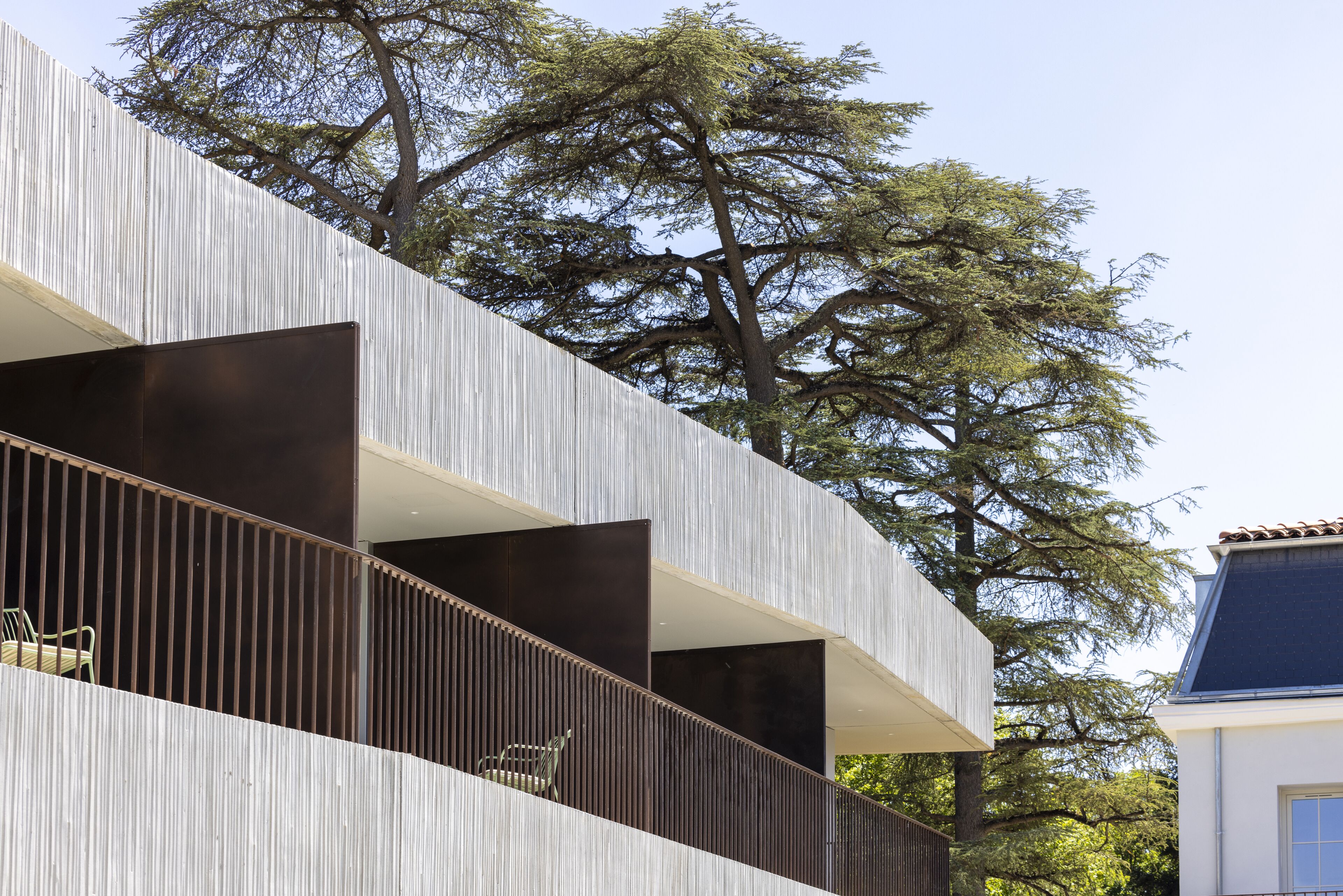 A modern building with a unique architectural design, featuring a series of balconies and a large tree in the background.