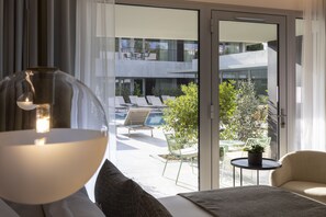 A modern hotel room with a large window, a bed, a round table with a plant, and a view of the outdoor pool and balcony. - Hôtel Spa Restaurant Villa Castellane by Germain Collection (Gréoux-les-Bains)