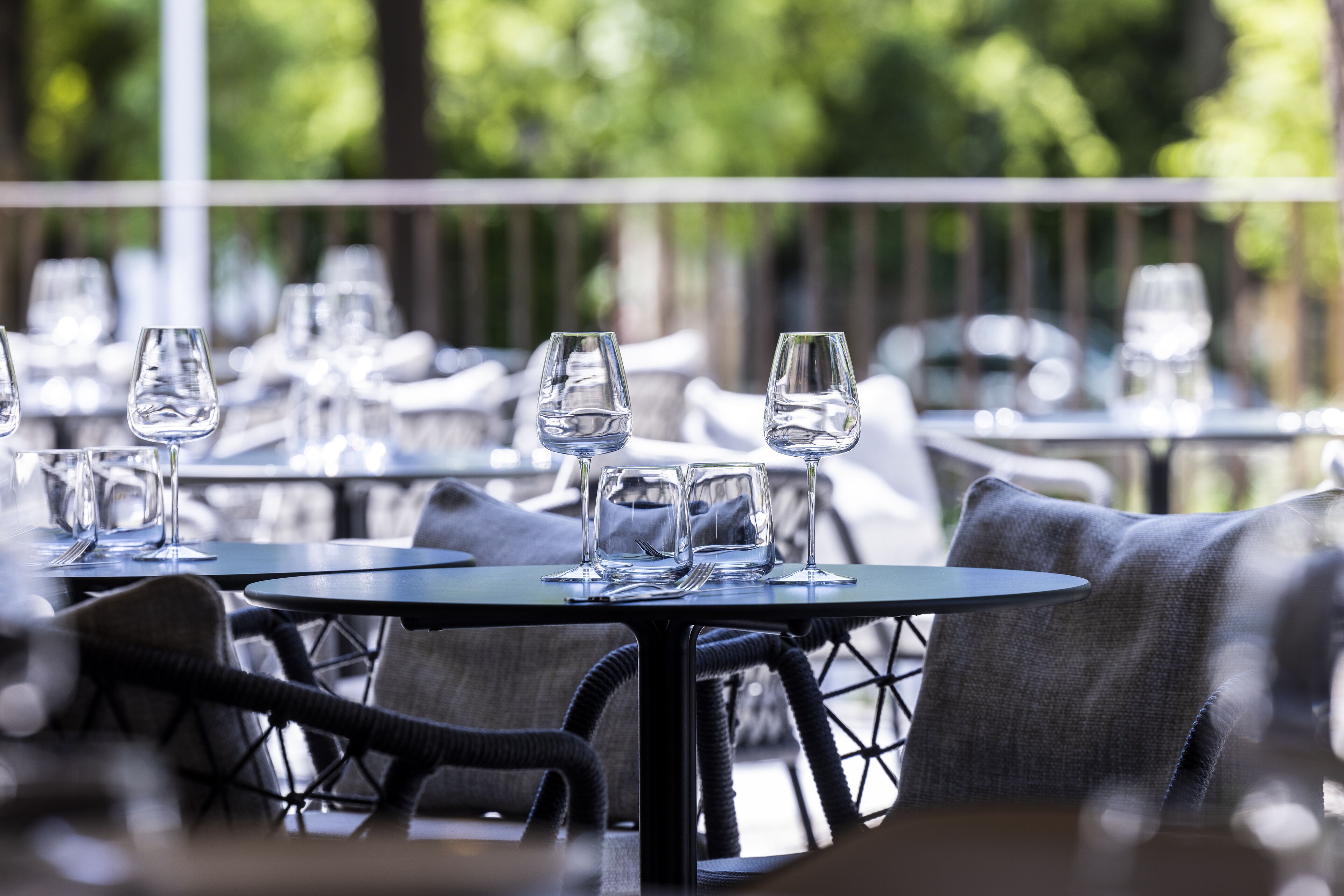 An outdoor dining area with round tables and chairs, surrounded by greenery.