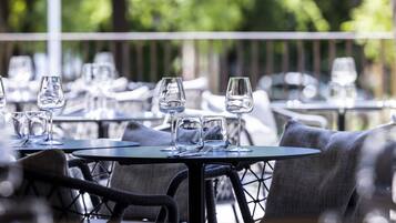 An outdoor dining area with round tables and chairs, surrounded by greenery.