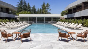 Un área de piscina moderna con sillas de descanso y mesas, rodeada de edificios y árboles.