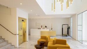 Un moderno vestíbulo de hotel con un mostrador de recepción, una escalera y un área de descanso con sofás amarillos.