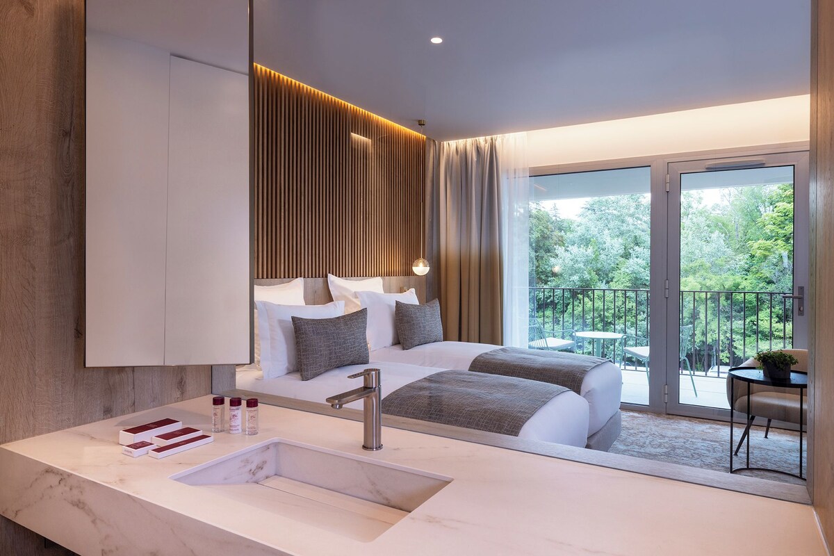 A modern hotel room with a large bed, a bathroom with a marble sink, and a balcony with outdoor furniture.