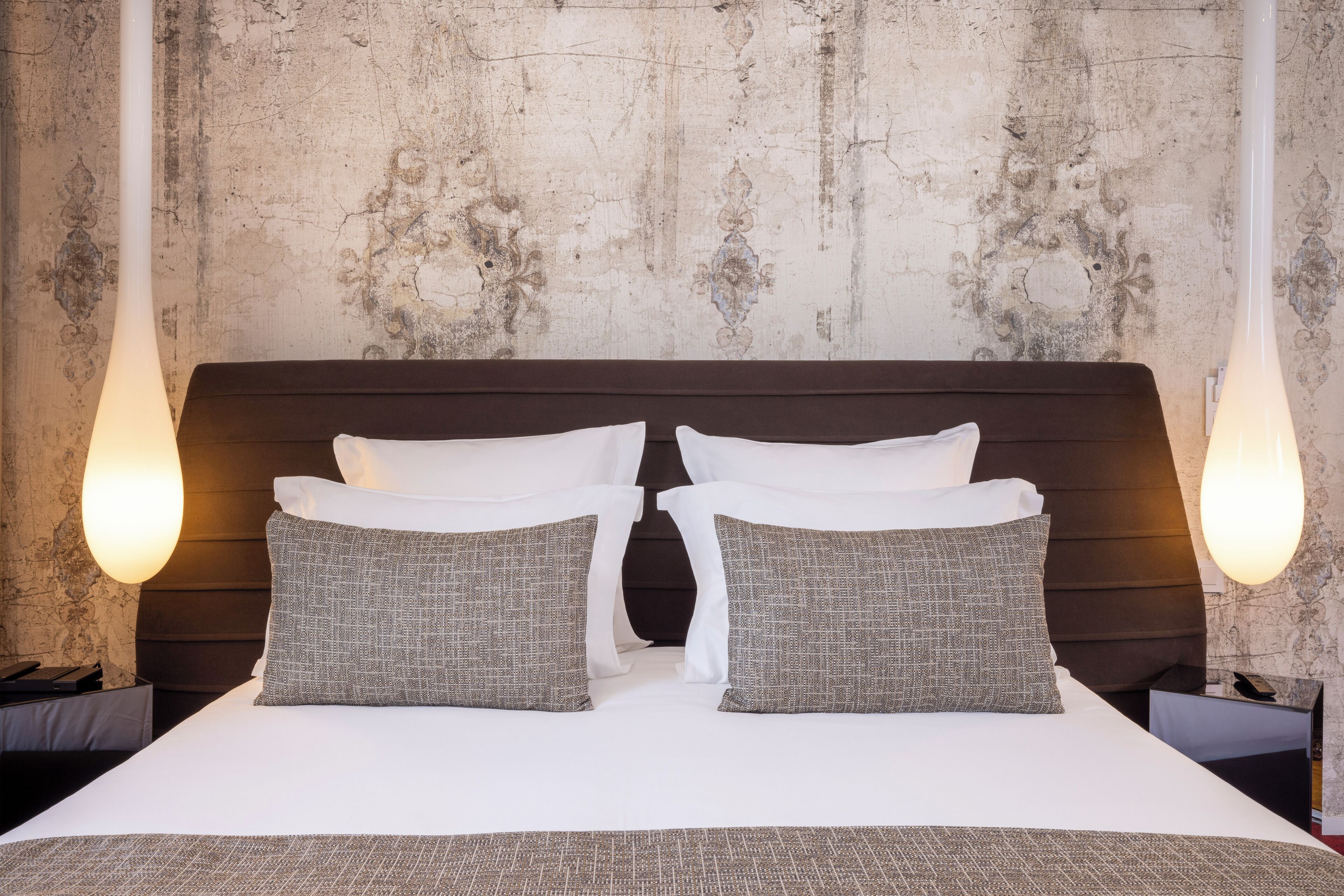 A neatly made bed with white and gray pillows, a dark headboard, and two bedside lamps.