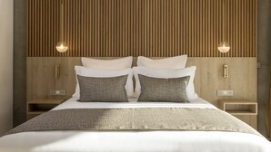 Una cama bien hecha con ropa de cama gris y blanca, dos mesitas de noche con lámparas y un cabecero de madera con listones.
