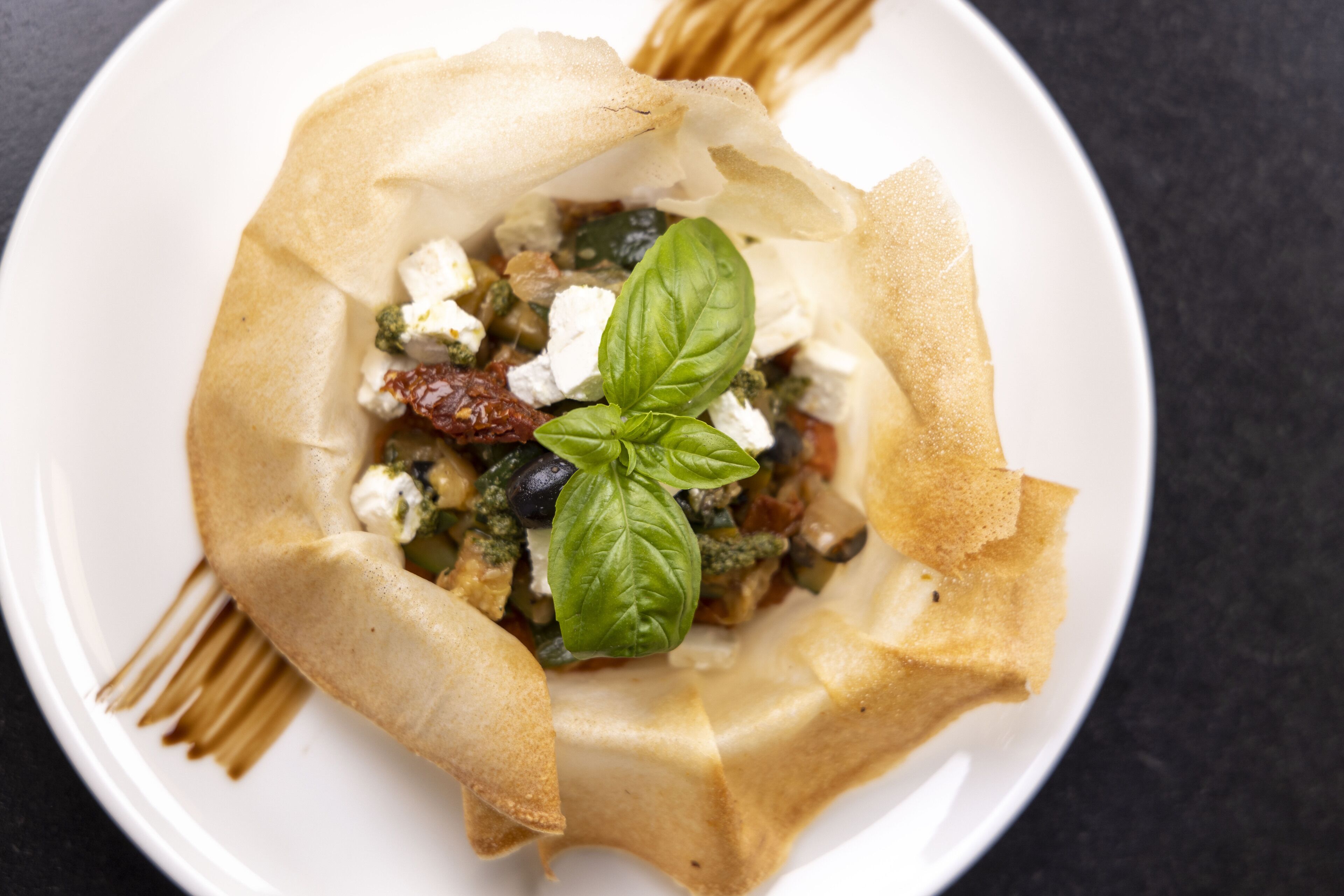A dish with a crispy, golden-brown crust, garnished with fresh basil and crumbled cheese, served on a white plate.