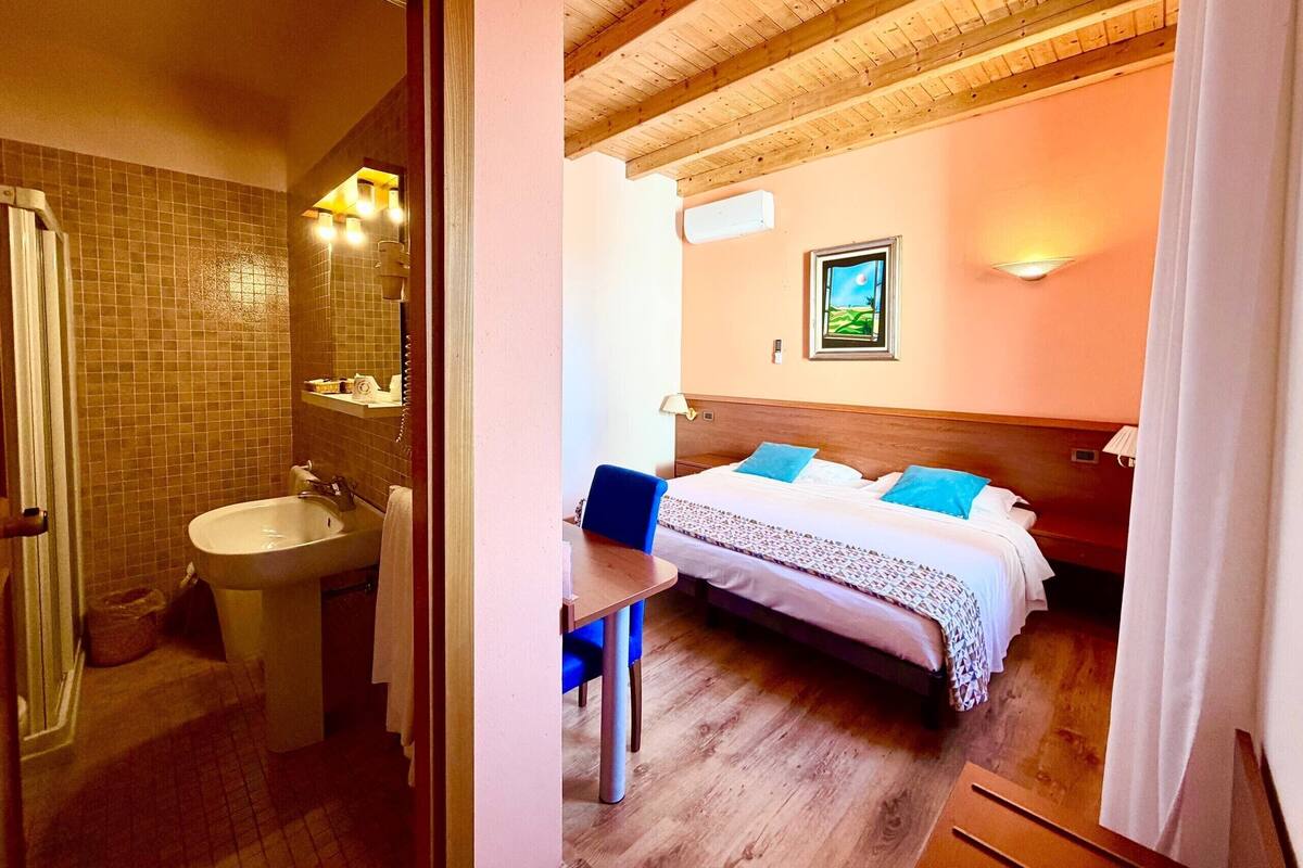 Une salle de bain avec un lavabo et un miroir, un plafond en bois, et un lit avec des oreillers bleus dans une chambre.