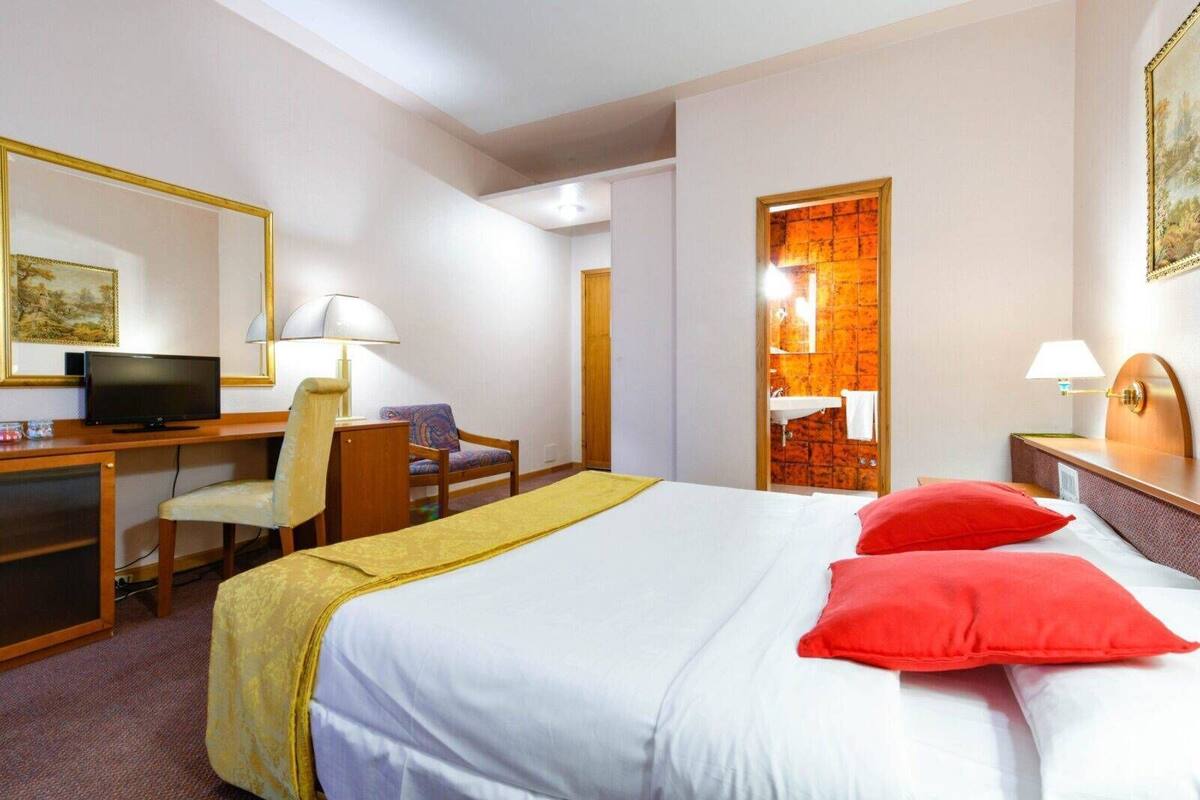 Une chambre d’hôtel avec un lit, un bureau et une chaise, un téléviseur et une salle de bain visible à travers une porte ouverte.