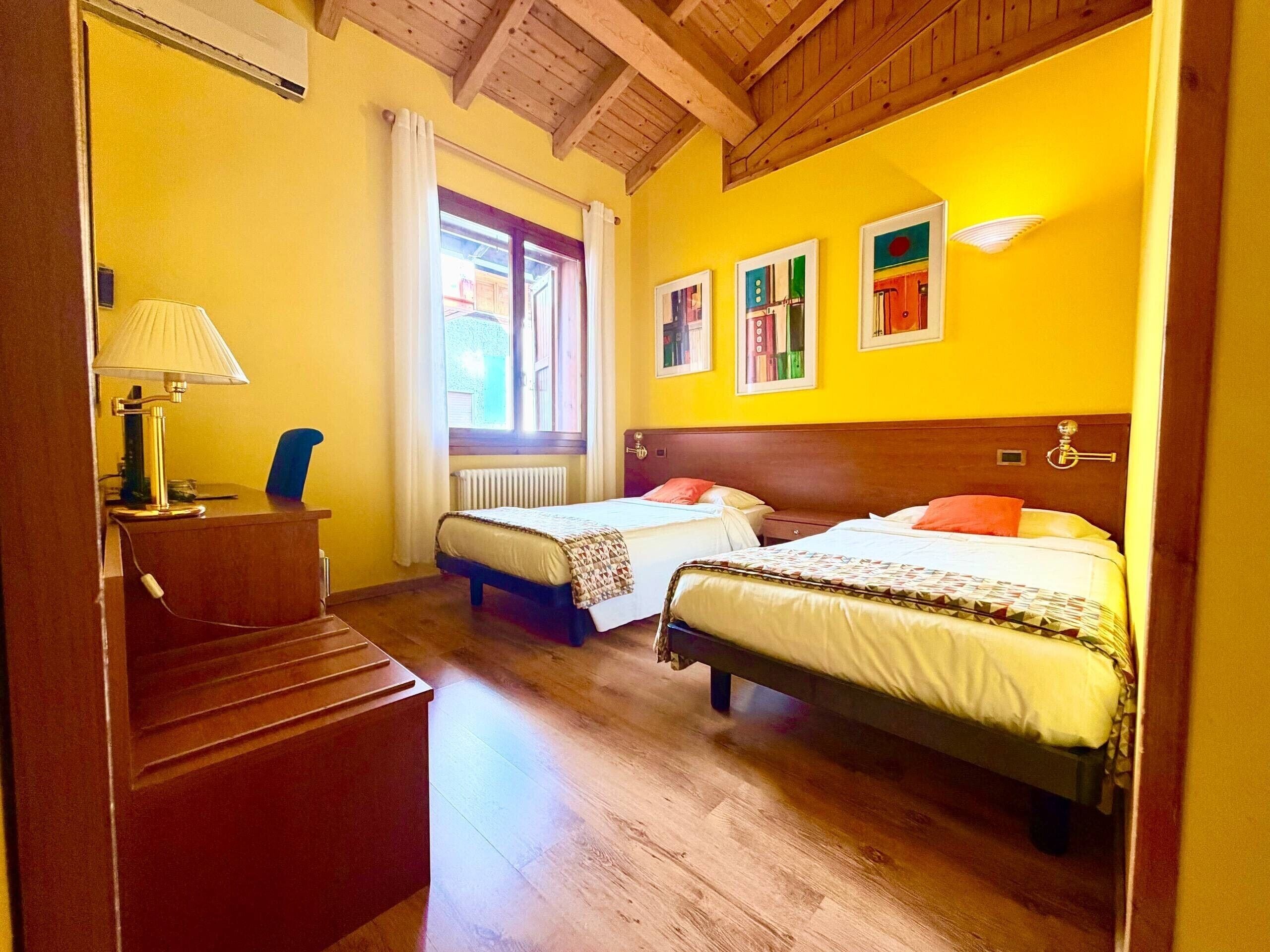 A hotel room with two beds, a desk, a lamp, and a window with curtains.