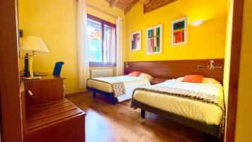 A hotel room with two beds, a desk, a lamp, and a window with curtains.