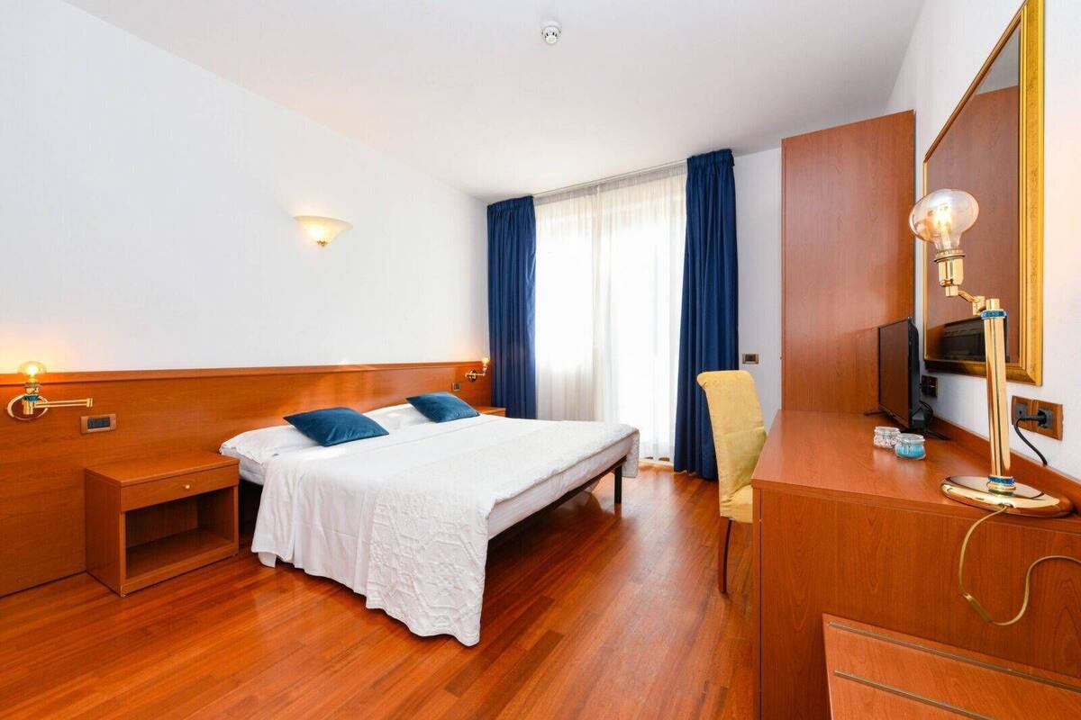 Une chambre d’hôtel avec un lit en bois, une table de chevet, un bureau avec une lampe, une chaise et un téléviseur.