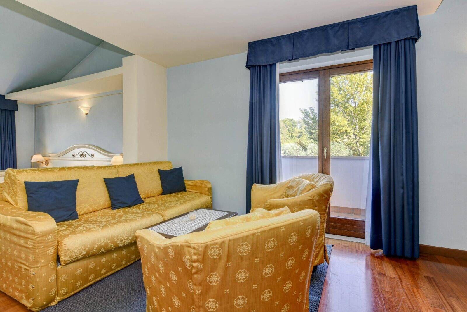 A room with a sofa, armchair, and a bed with a headboard.