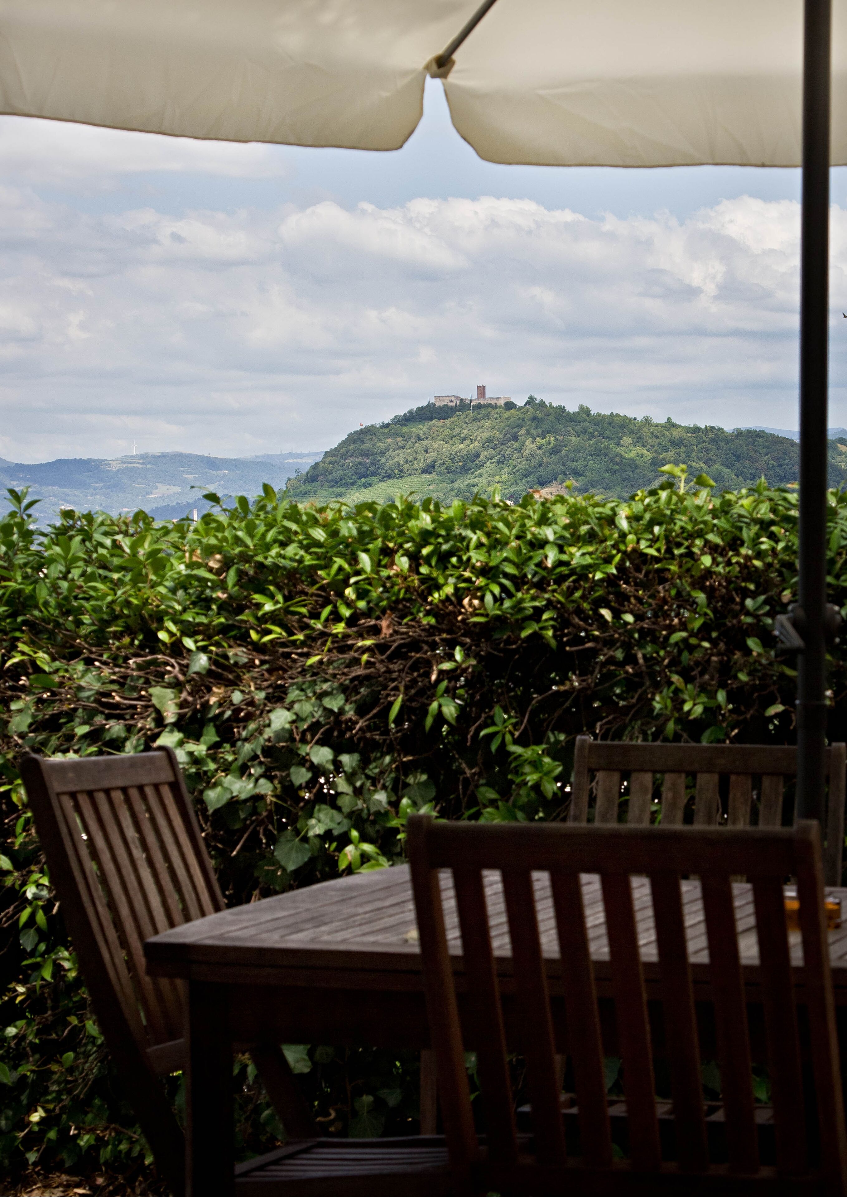 A table and chairs under a canopy with a view of a hill and distant buildings.