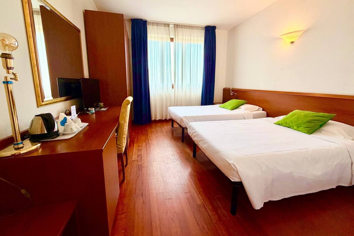 Une chambre d’hôtel avec deux lits simples, un bureau avec une chaise, une télévision et un grand miroir.