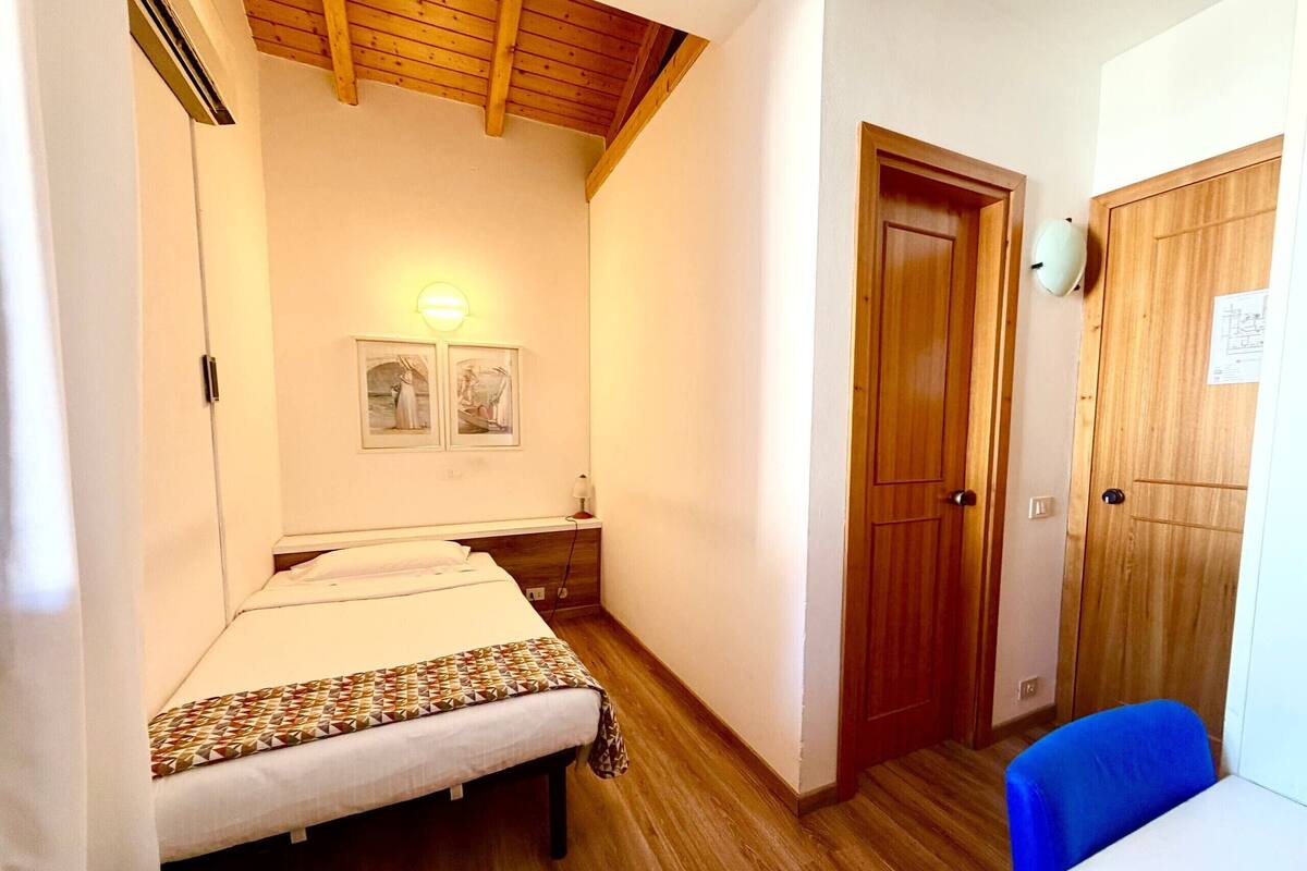 Une chambre à coucher avec un lit, un plancher en bois, une porte et un luminaire fixé au mur.