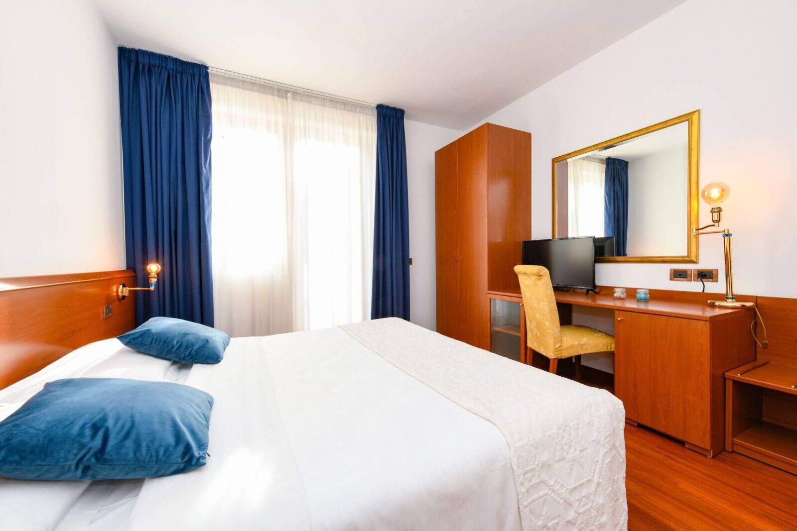 Une chambre d’hôtel équipée d’un lit, d’un bureau, d’une chaise, d’une télévision, d’un miroir et d’une lampe.