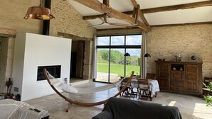 A spacious room with a hammock, a fireplace, a dining area, and a view of the outdoors. - Converted barn/gergergerie in the countryside. (Castelner)