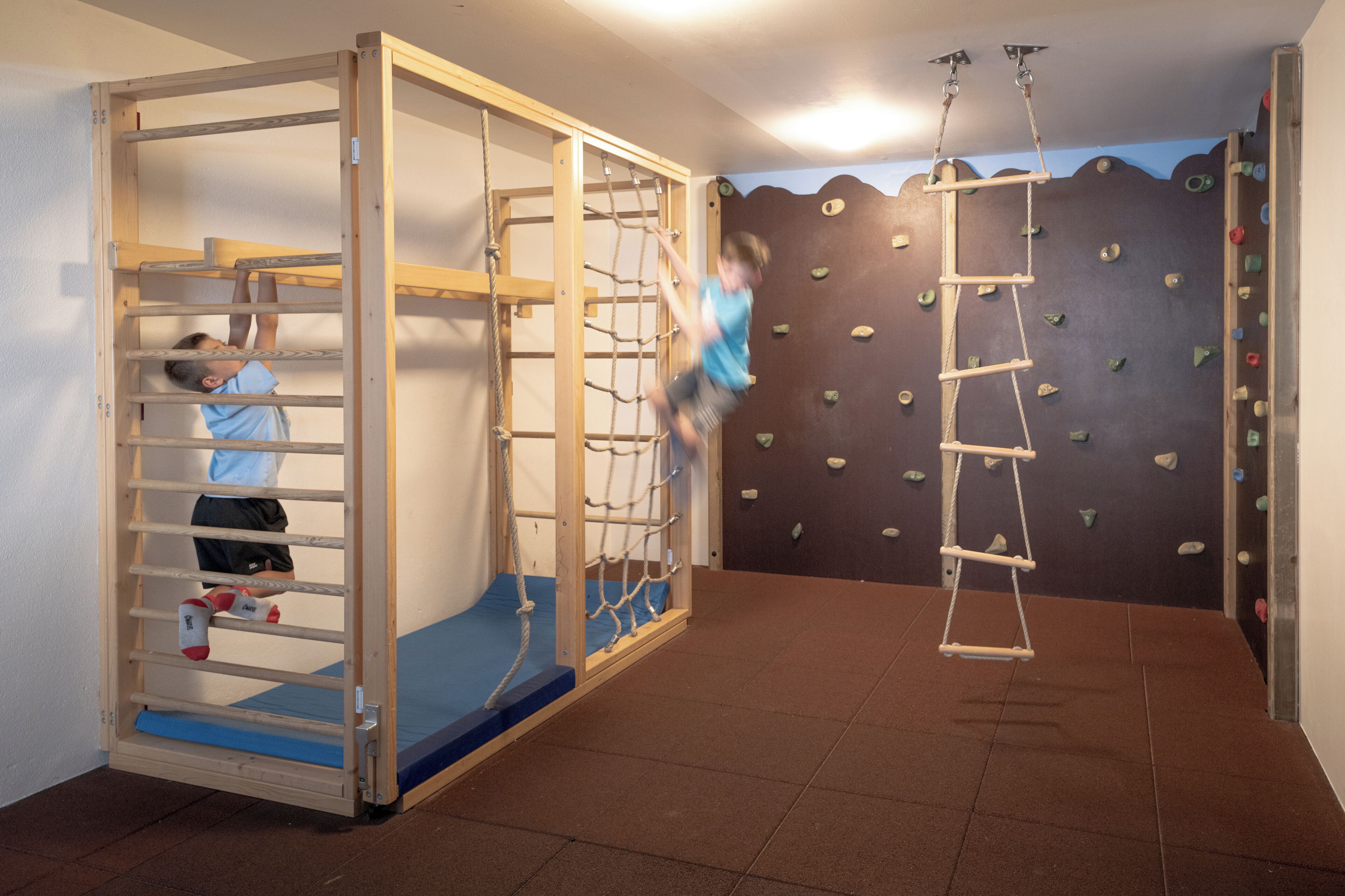 Una sala de juegos con una pared de escalada, una estructura de madera para jugar y una escalera colgante.