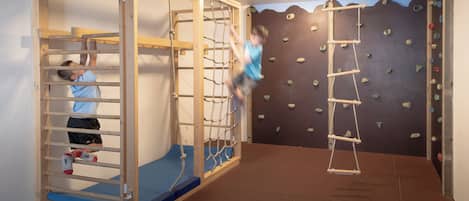 A playroom with a climbing wall, a wooden play structure, and a hanging ladder.