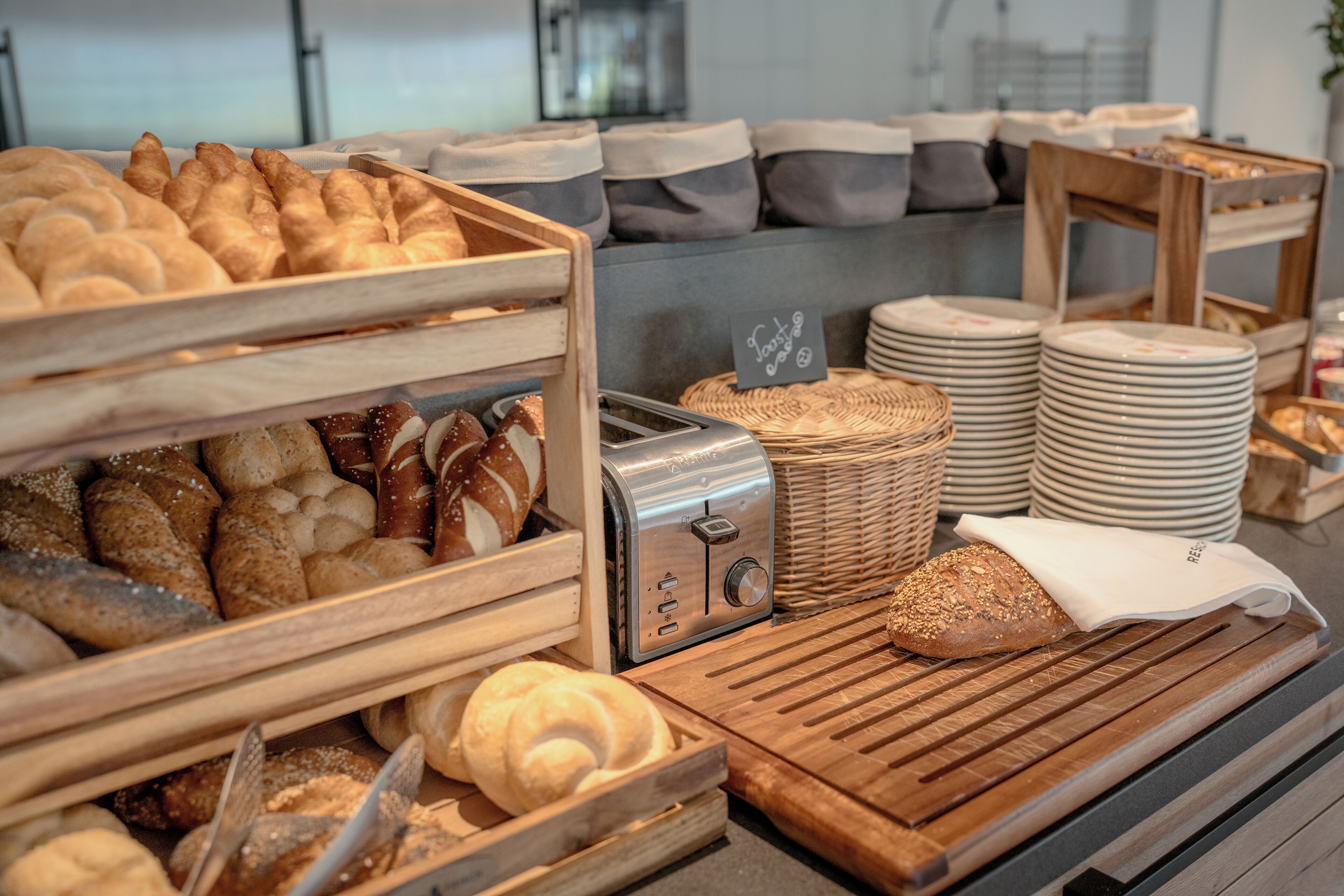 A bakery display with various breads and pastries, a toaster, and stacked plates.