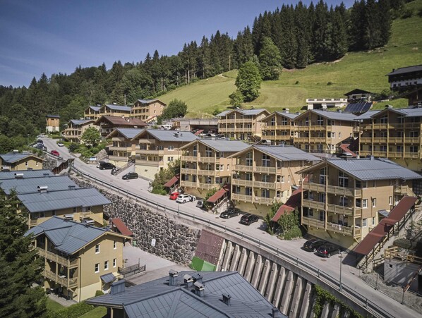 A cluster of chalet-style buildings with balconies, a central road, and a backdrop of forested hills. - AlpenParks Ferienresort Rehrenberg (Viehhofen)