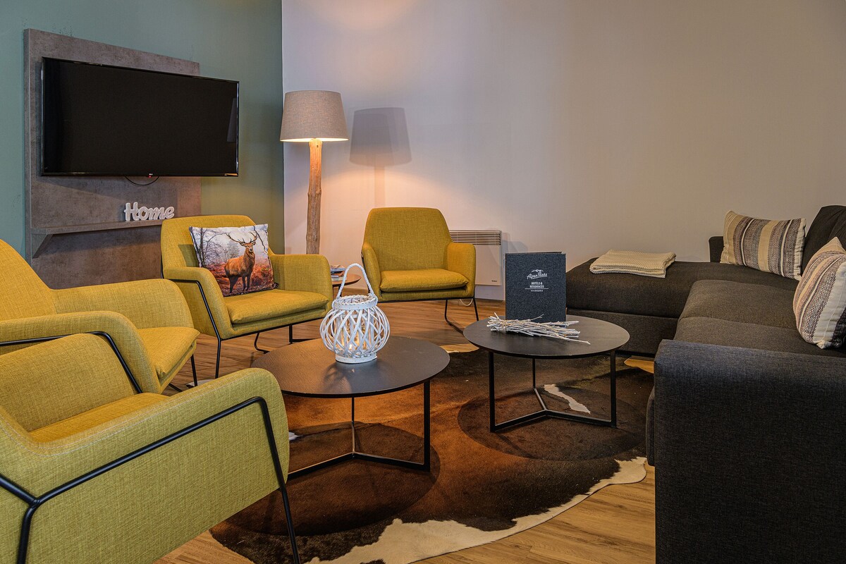 A modern living room with a flat-screen TV, two armchairs, a sofa, a coffee table, and a floor lamp.