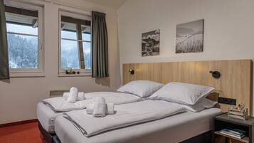 A double bed with white linens and towels, a bedside table with a lamp, and two framed pictures on the wall.