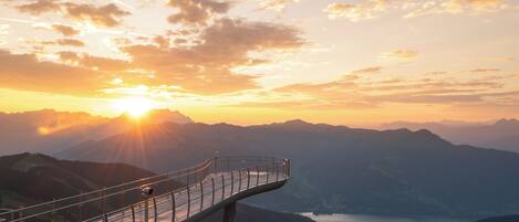 A scenic overlook with a metal railing, overlooking a valley and a lake during sunset.