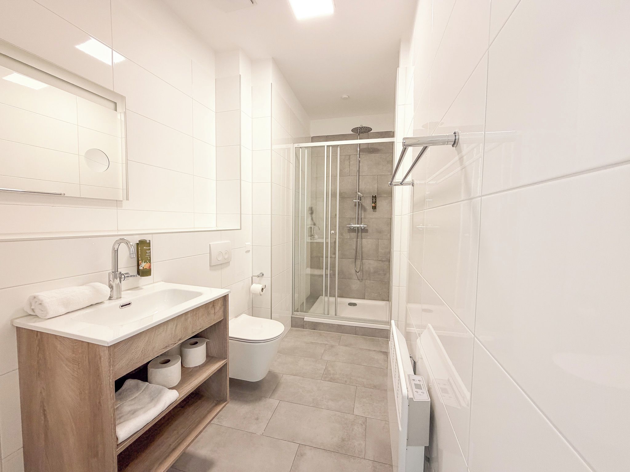 A modern bathroom with a glass-enclosed shower, a wooden vanity, and a toilet.
