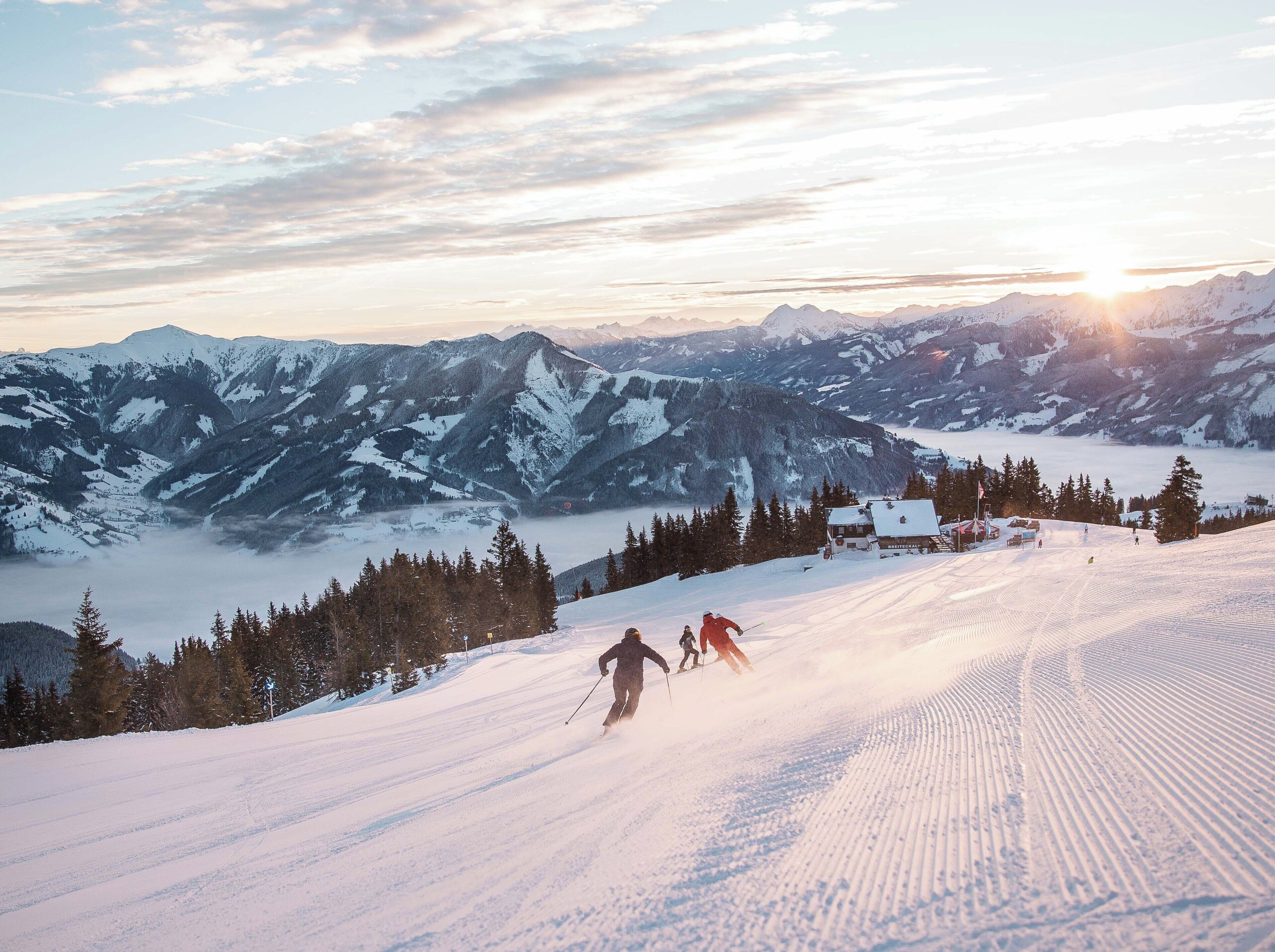 Un paysage de montagne enneigé avec des skieurs, un chalet et un ciel dégagé.
