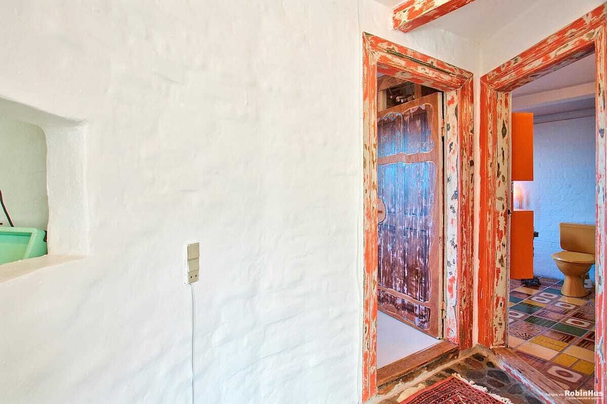 A room with a white wall, a door with a colorful frame, a green object on the wall, and a tiled floor.