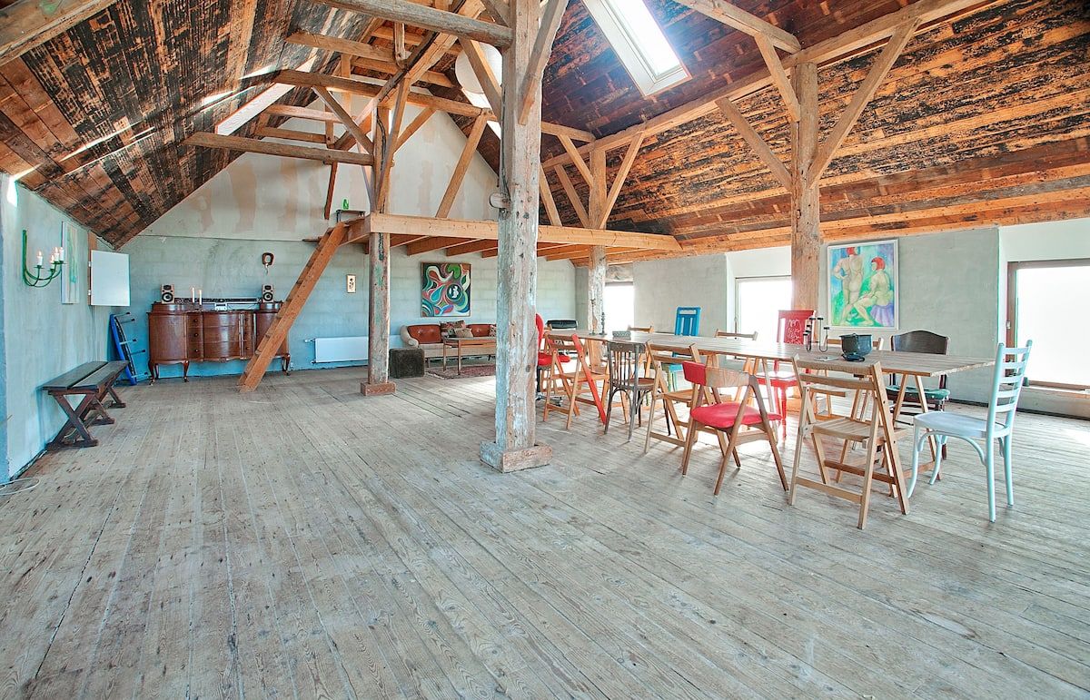 Ein geräumiges Loft mit freiliegenden Holzbalken, einem Essbereich mit Holztischen und -stühlen sowie Kunstwerken an den Wänden.