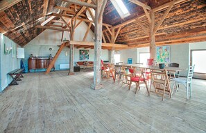 A spacious loft with exposed wooden beams, a dining area with wooden tables and chairs, and artwork on the walls.