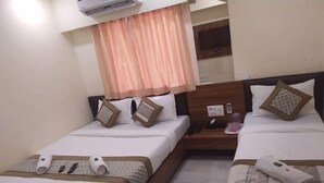 Habitación de hotel con dos camas, cada una con ropa de cama blanca y almohadas decorativas. Se observa un mesita de noche con un teléfono y una pequeña mesa con una taza y una caja de pañuelos.