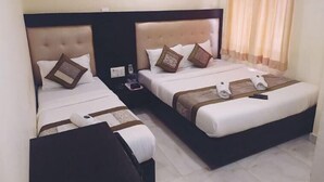 Habitación de hotel con dos camas, cada una con cabecera, almohadas y una manta. Hay una mesita de noche con un teléfono y una botella.