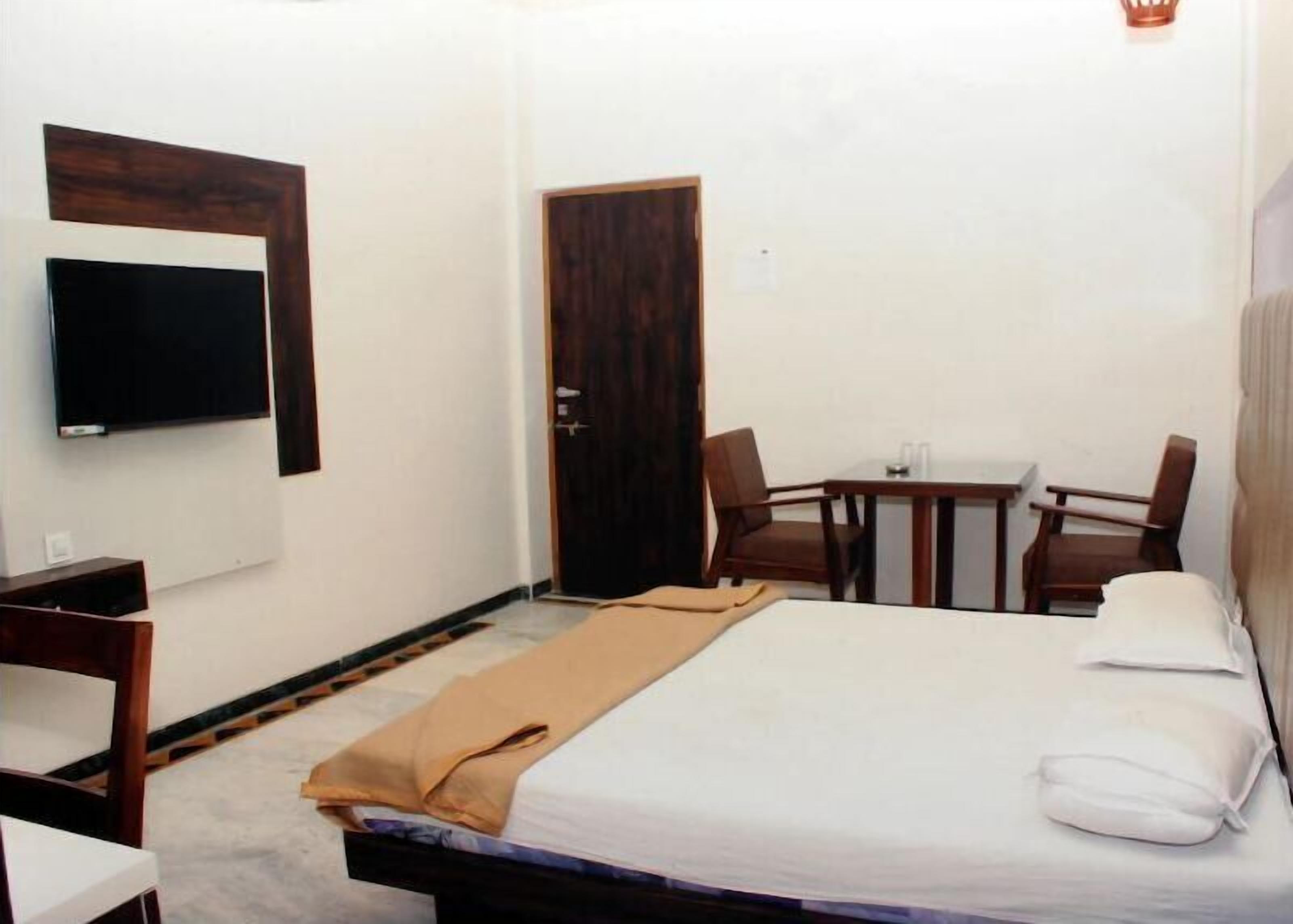 Una habitación de hotel con cama, televisor montado en la pared, una mesita con sillas y una puerta.