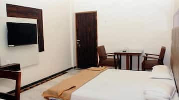 A hotel room with a bed, a TV mounted on the wall, a small table with chairs, and a door.