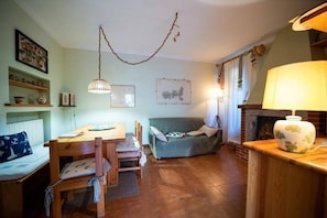 Ein gemütliches Wohnzimmer mit einem Esstisch, Stühlen, einer Couch, einem Kamin und Wandbildern.