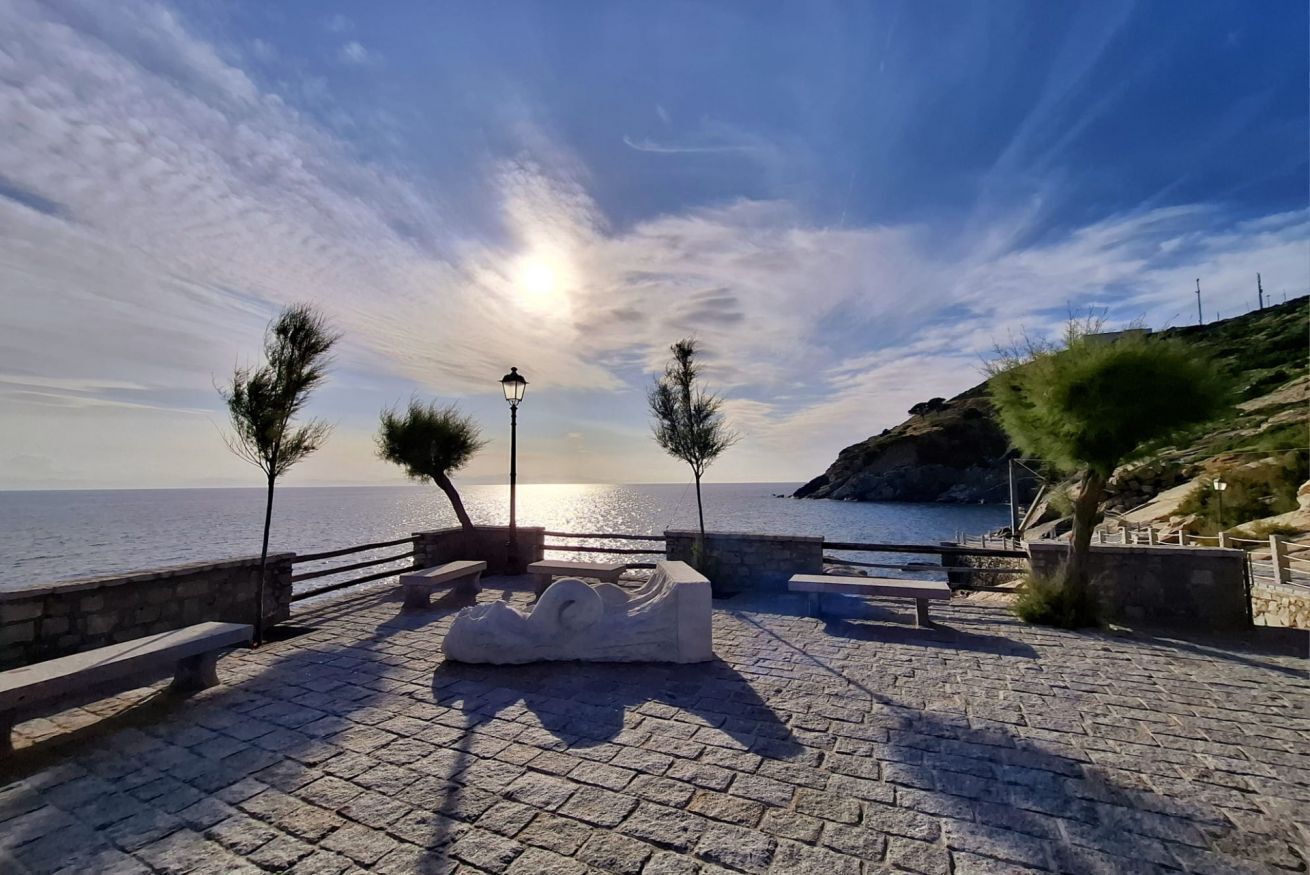 Une promenade en bord de mer, dallée, agrémentée de bancs, d’une sculpture et d’un lampadaire.
