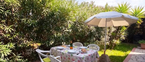 An outdoor patio with a table set for dining, surrounded by lush greenery.