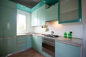 A kitchen with teal cabinets, a gas stove, and a window. - La Casa di Rosetta - Two-room Apartment (Marina di Campo)