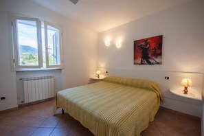 A bedroom with a bed, two bedside lamps, a radiator, and a window with an open shutter.