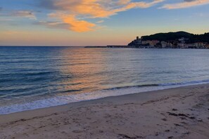 A beach with a calm sea, a sandy shore, and buildings in the background.