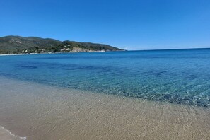 Una playa con agua cristalina, una orilla arenosa y un paisaje montañoso al fondo.