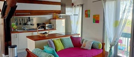 A cozy room with a wooden bed, a kitchen area with basic appliances, and a window with curtains.