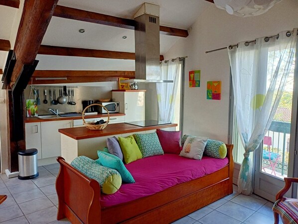 A cozy room with a wooden bed, a kitchen area with basic appliances, and a window with curtains.