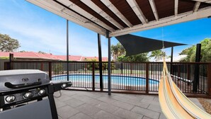 A covered patio with a barbecue grill, a hammock, and a view of a swimming pool.