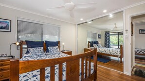 A bedroom with a wooden bed, bedside tables, a ceiling fan, and a large mirror reflecting the room.