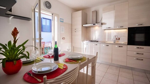 A modern kitchen with white cabinets, a black oven, and a dining area with a table set for two. - Aricipelgo - Ponza apartment (Marina di Campo)