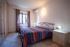 Un dormitorio con cama, mesita de noche, lámpara y ventana con cortinas.